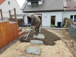 Muž urovnávající půdu v okolí čedičových nášlapů vedle bazénu